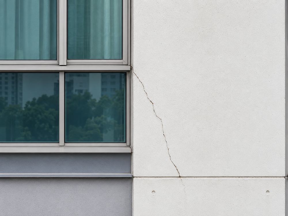 Close-up of a hairline crack running diagonally across a rendered concrete wall beside a window